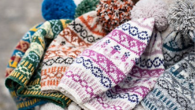 Pile of different coloured knitted bobble hats with intricate patterns 